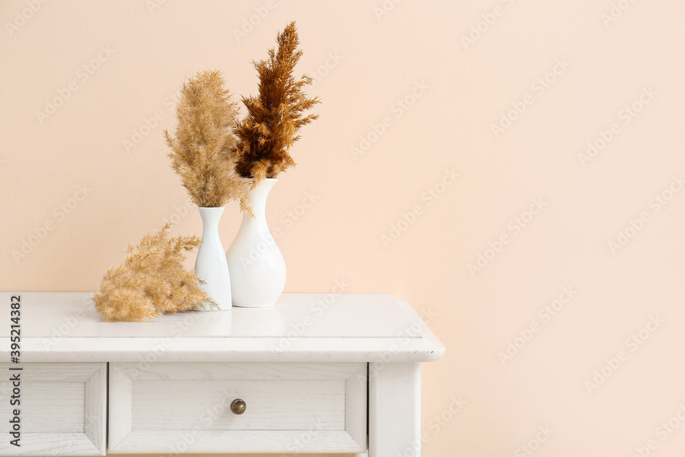 Beautiful vases with pampas grass on light table against color background