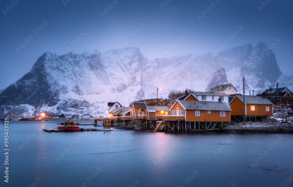 Rorbu on sea coast and snow covered mountain in fog at dusk. Lofoten islands, Norway. Moody winter l