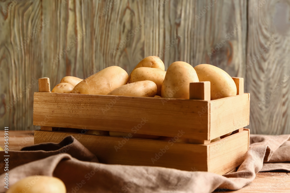 Wooden crate with raw potatoes on wooden table