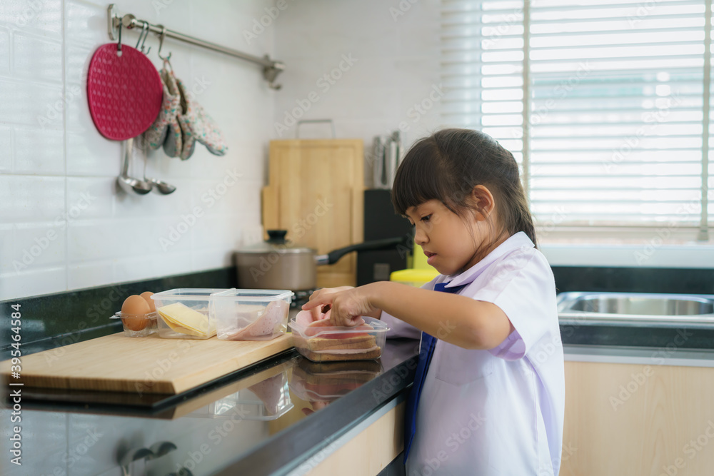 穿制服的亚洲小学生女孩在早校食堂为午餐盒做三明治