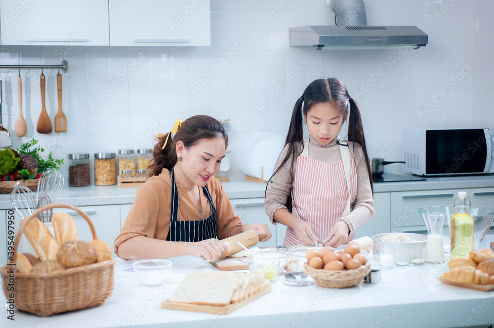 快乐的亚洲妈妈和可爱的女儿在厨房里帮忙揉面团做面包。