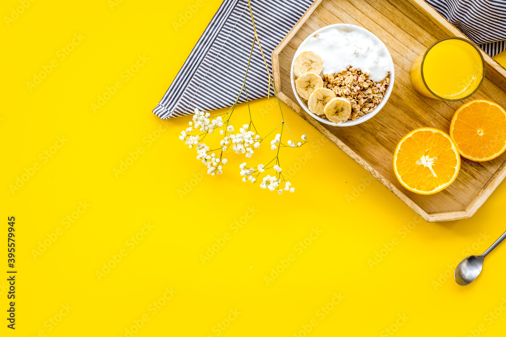 Healthy granola with banana and orange juice for colorful breakfast on yellow background top view mo