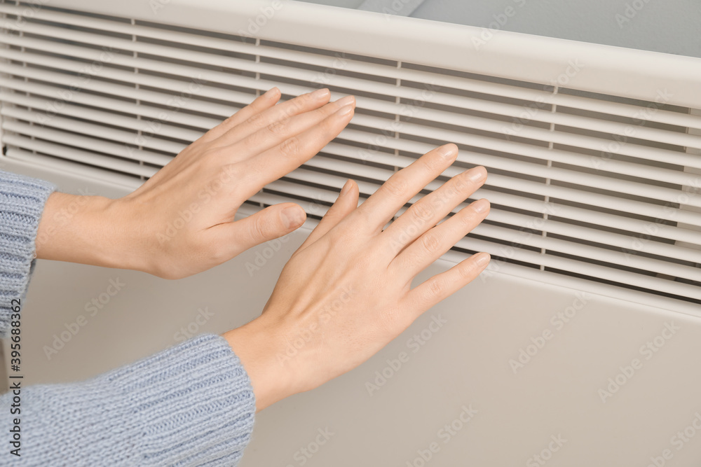 Woman warming hands at radiator. Concept of heating season