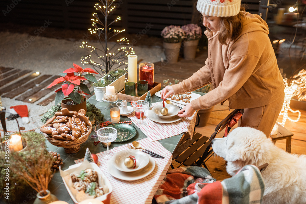 Woman serving and decorating a festive dinner table on the christmas eve outdoors on the terrace