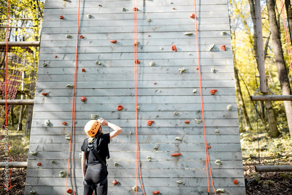 Young woman in sportswear and safety equipment looking on the climbing wall before climbing. Wide vi