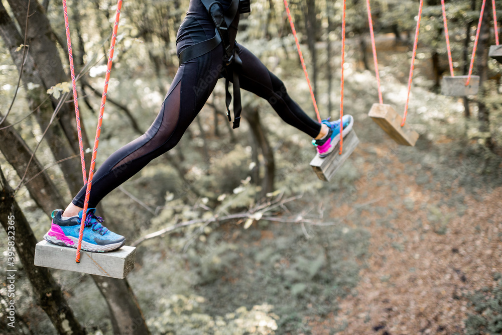 Young well-equipped woman having an active recreation, climbing ropes in the park with obstacles out