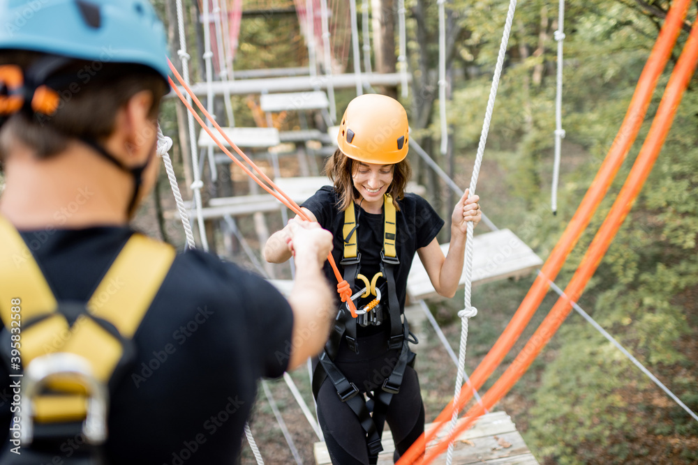 Well-equipped man and woman having an active recreation, climbing ropes in the park with obstacles o