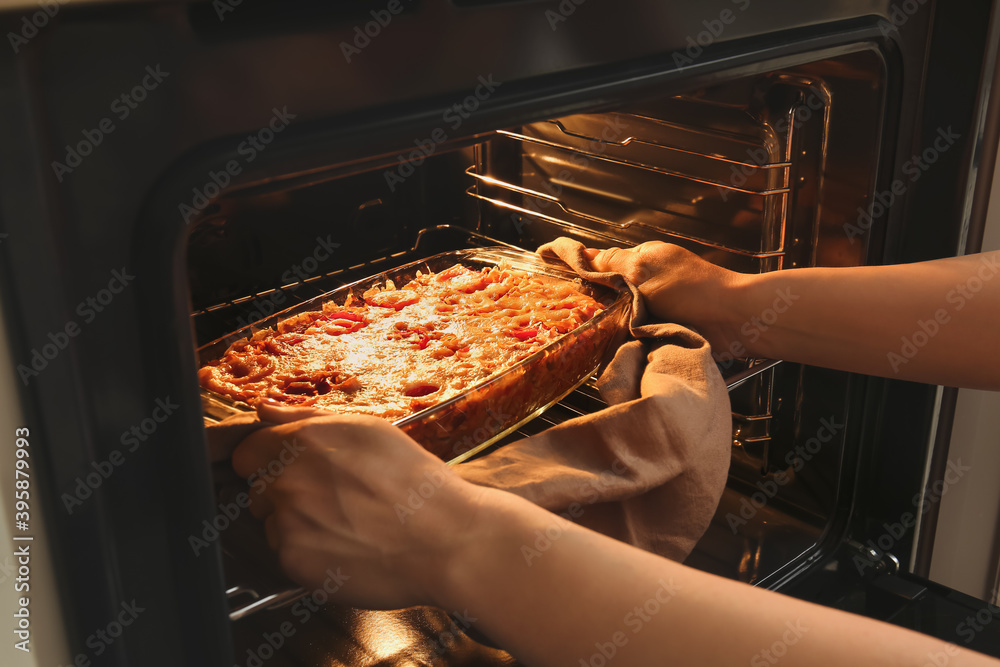 Woman taking baking dish with tasty rice casserole out of oven