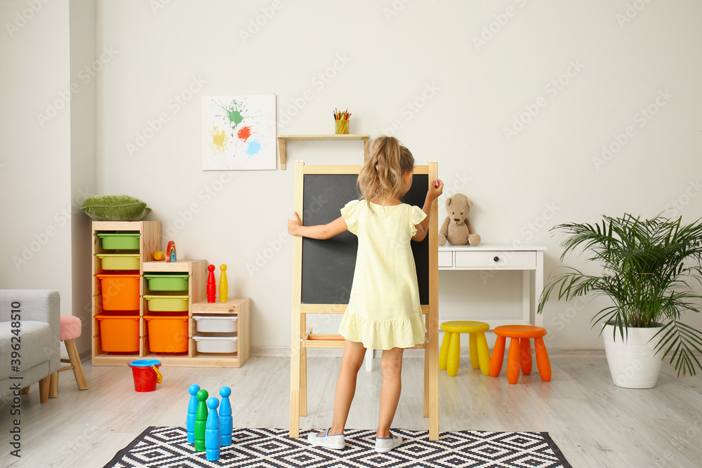 Cute little girl drawing on blackboard in kindergarten