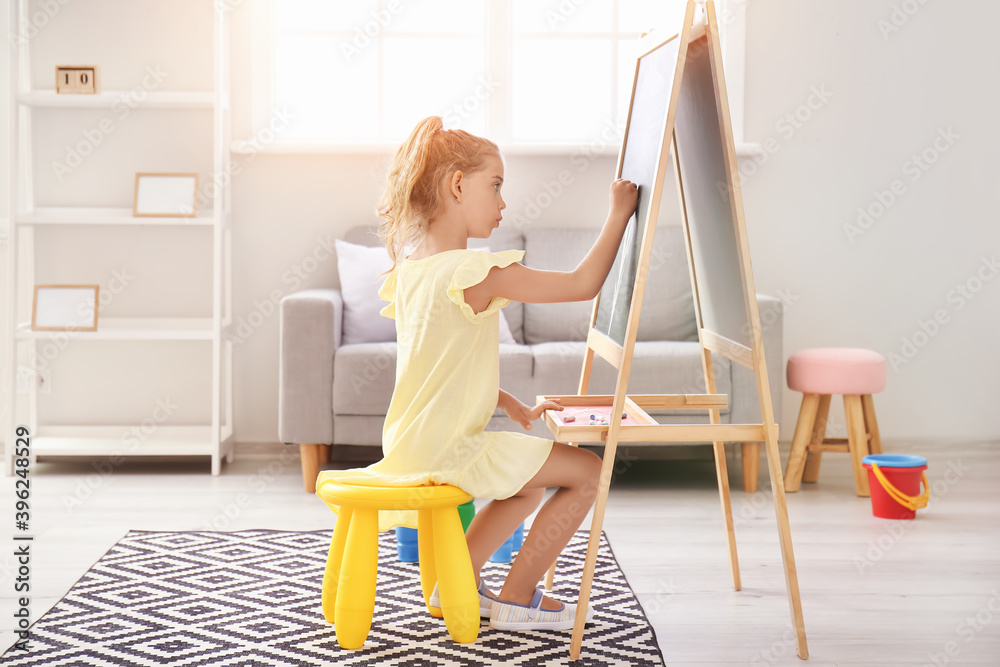 Cute little girl drawing on blackboard in kindergarten