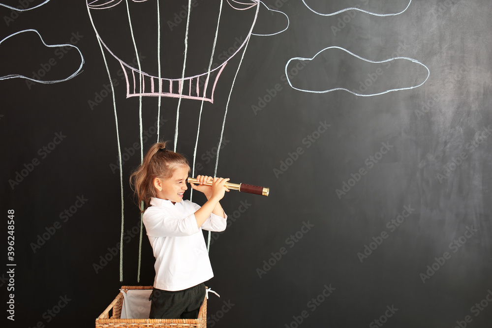 Cute little girl watching in spyglass on black wall with drawn hot air balloon