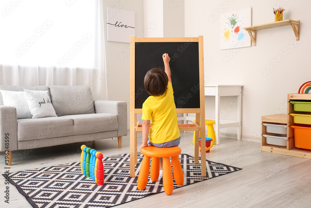 Cute little boy drawing on blackboard in kindergarten