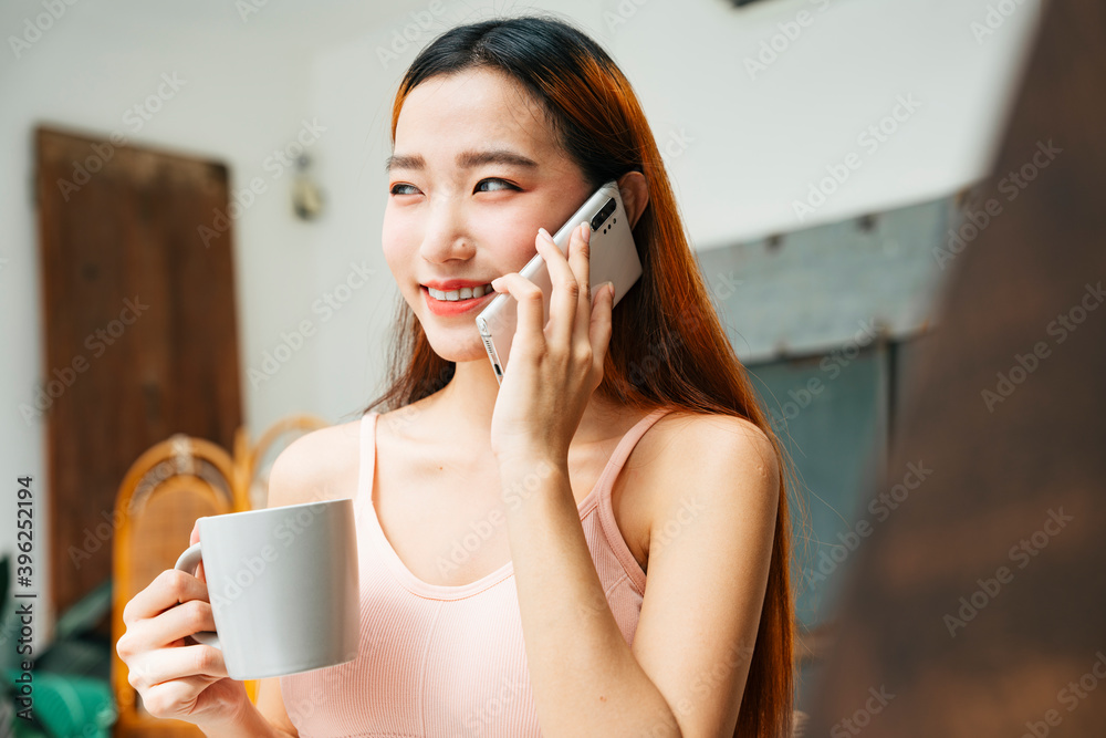 一位年轻漂亮的亚洲美女，拿着一杯咖啡和智能手机。