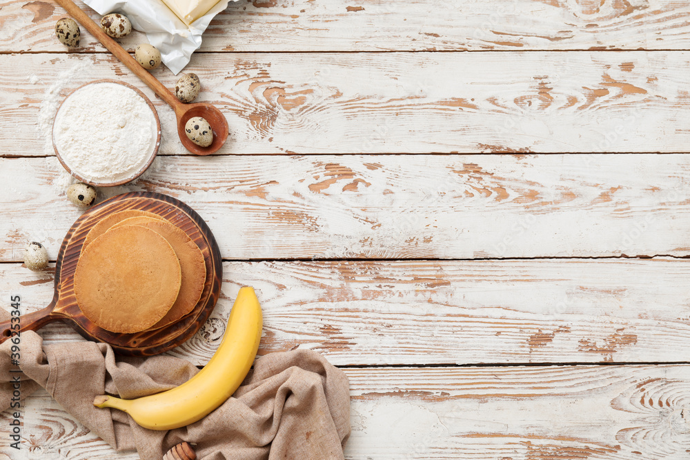 Tasty banana pancakes with ingredients on white wooden background