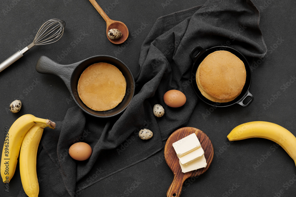 Tasty banana pancakes with ingredients on dark background