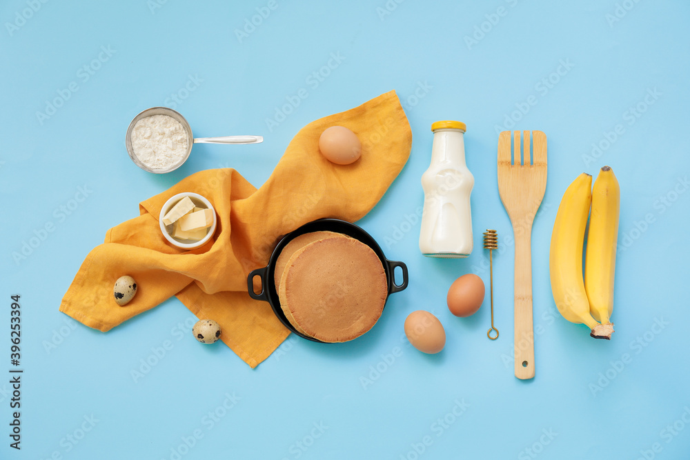 Tasty banana pancakes with ingredients on color background