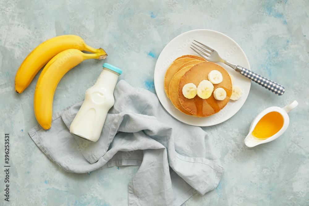 Plate with tasty banana pancakes, milk and honey on color background