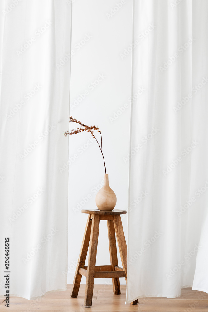 Dry Forsythia branch in a wooden vase on a stool by a white curtain