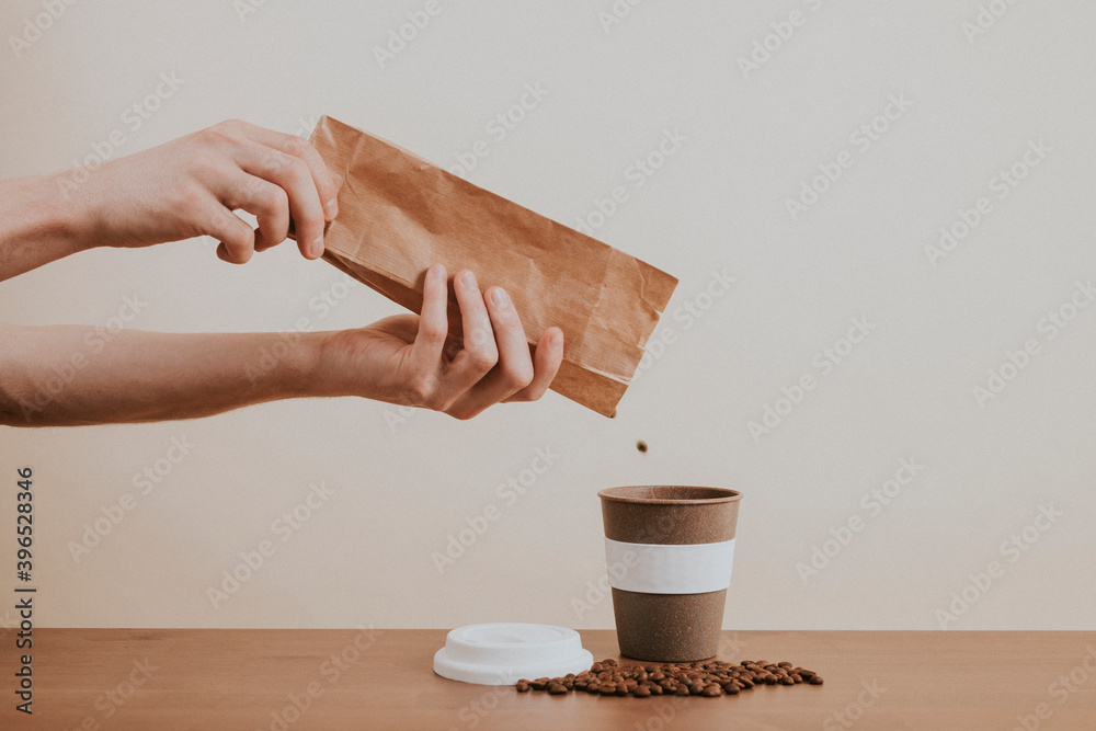 Hand pouring coffee beans from a paper bag into a coffee cup