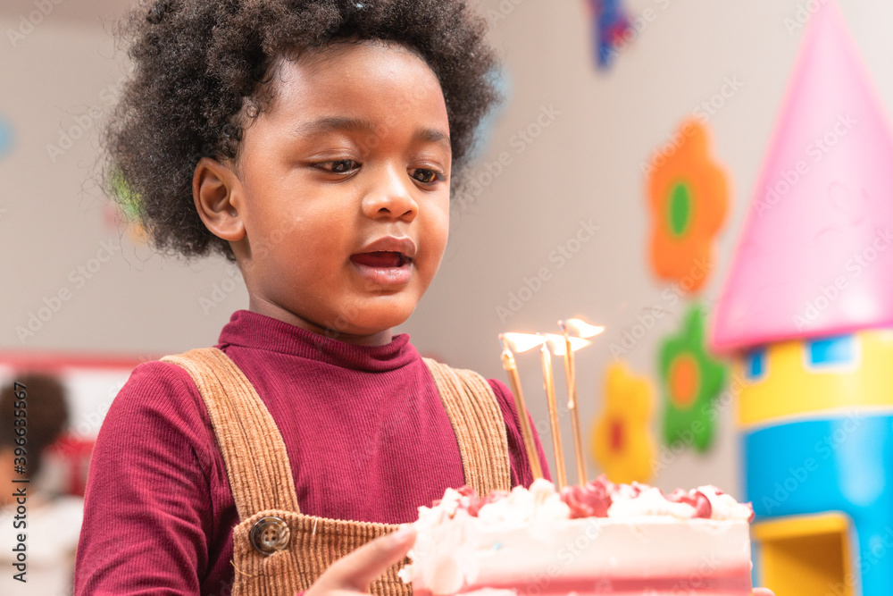 Happy little black boy holding birthday cake ready to blowing candles. African American kid with afr