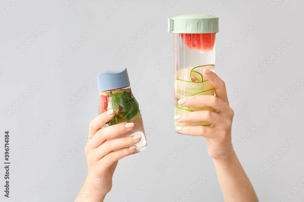 Female hands and bottles of infused water with citruses on light background