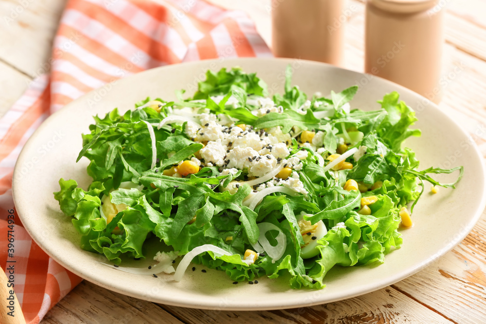 Plate with tasty arugula salad on wooden table