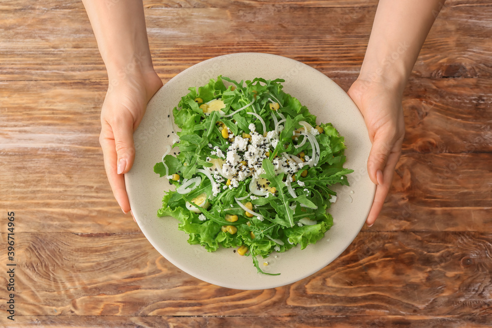 Female hands and plate with tasty arugula salad on wooden background