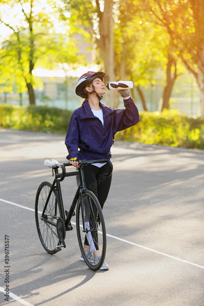 Female cyclist with bicycle drinking water outdoors