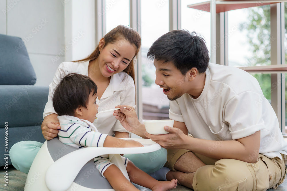 亚洲父亲用勺子给6个月大的男婴喂固体食物，母亲坐在旁边