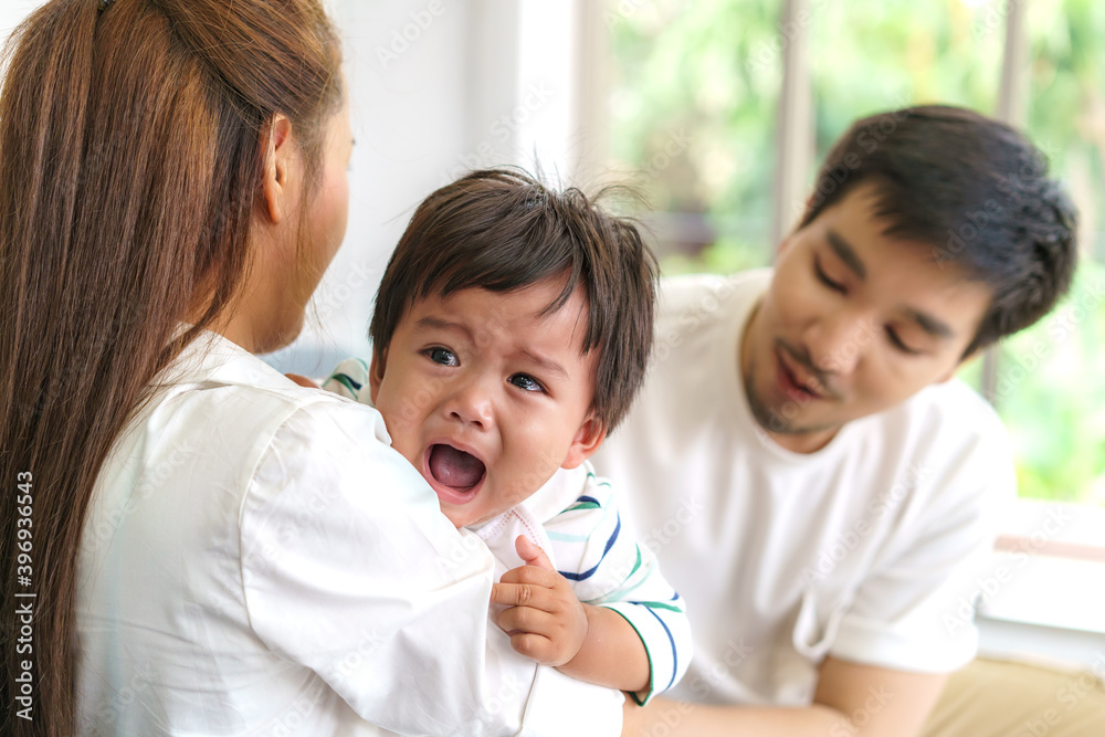 Asian Parents with mother and father trying to calm down crying infant son in living room at home.