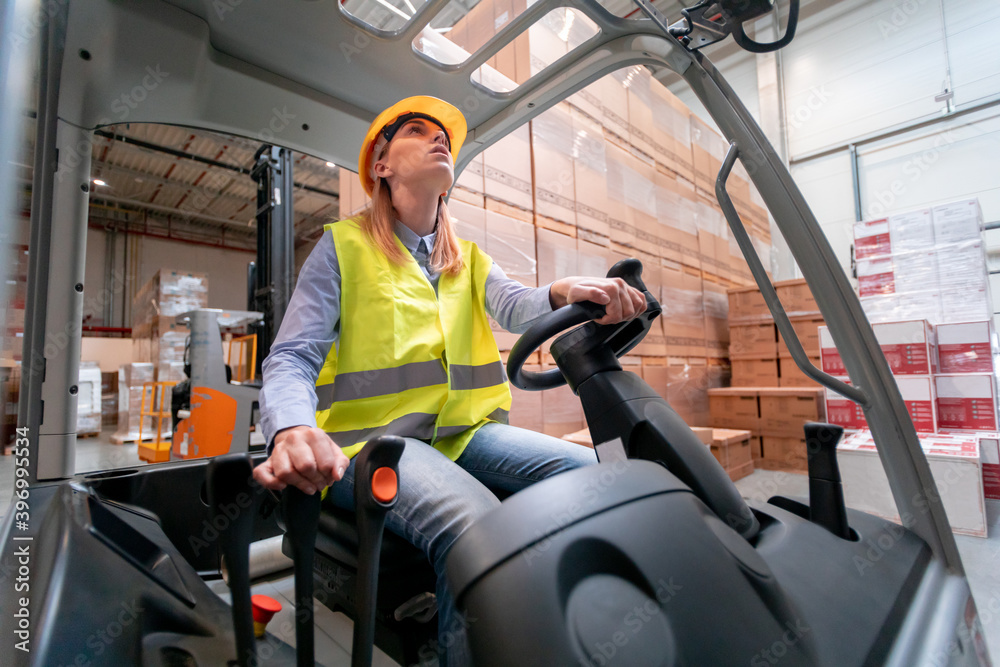 Focused female warehouse worker with forklift at work