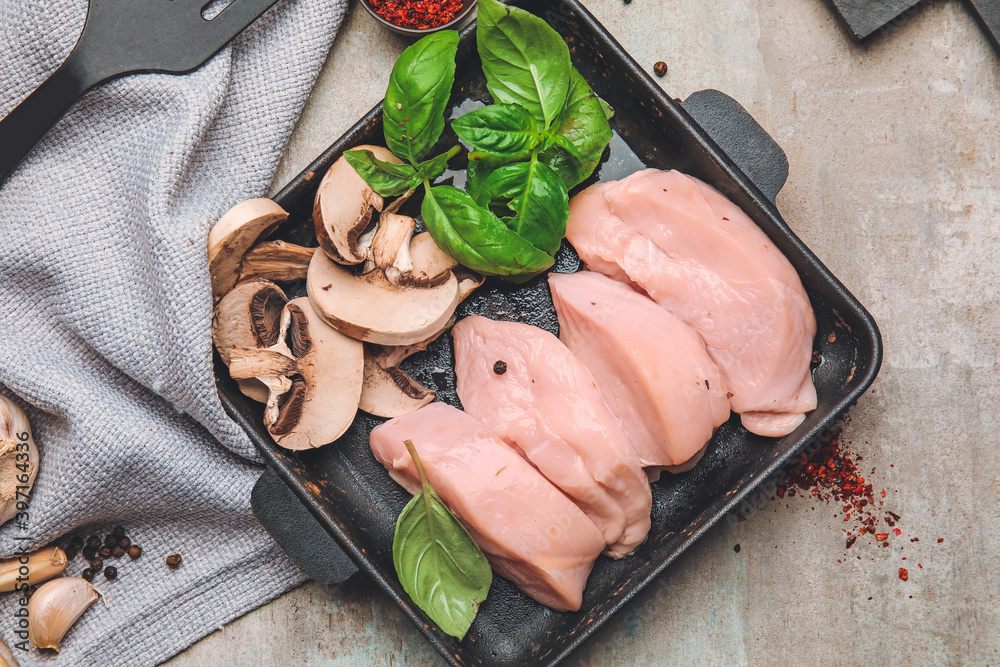 Ceramic plate with raw cut chicken fillet, mushrooms and basil on table