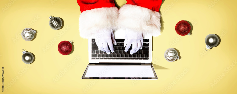 Santa Claus using a laptop computer with Christmas baubles from above