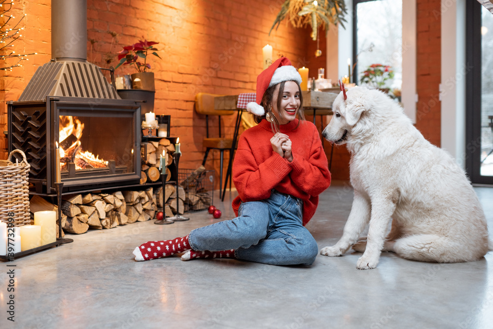 一个年轻的女人和她可爱的白狗在快乐的新年假期里坐在家里的壁炉旁