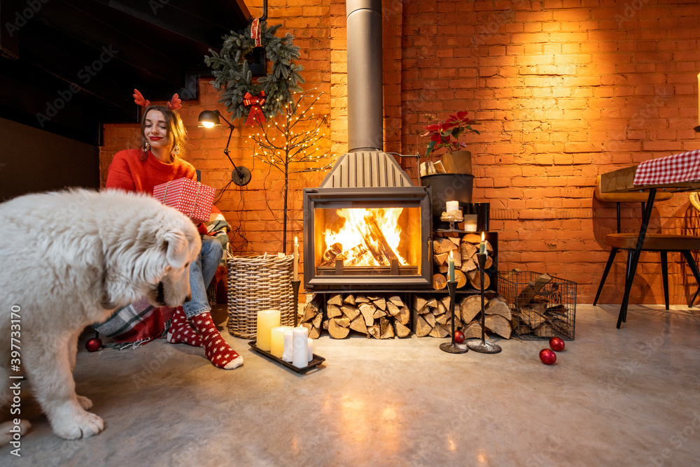 Young woman with her cute white dog during a happy New Year holidays sitting by a fireplace at home