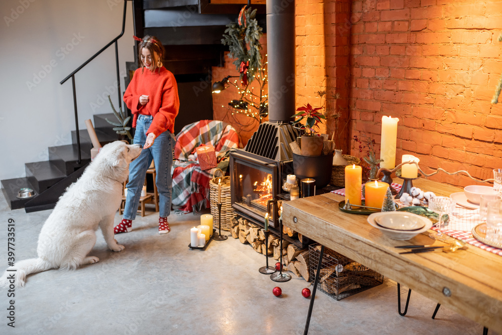 Young woman with her cute dog preparing for a New Year holidays by the fireplace and dining table at