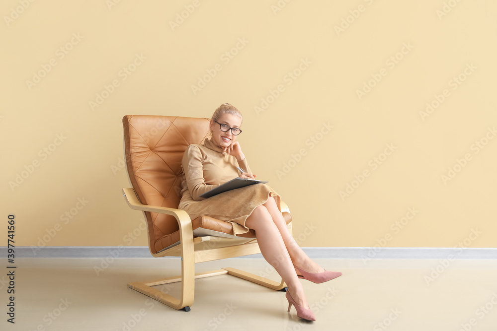 Portrait of female psychologist sitting in armchair near color wall