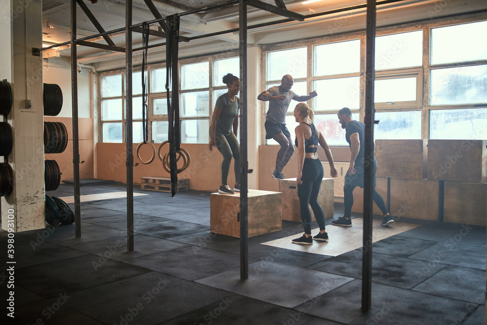 Diverse people doing box jumps together in a gym