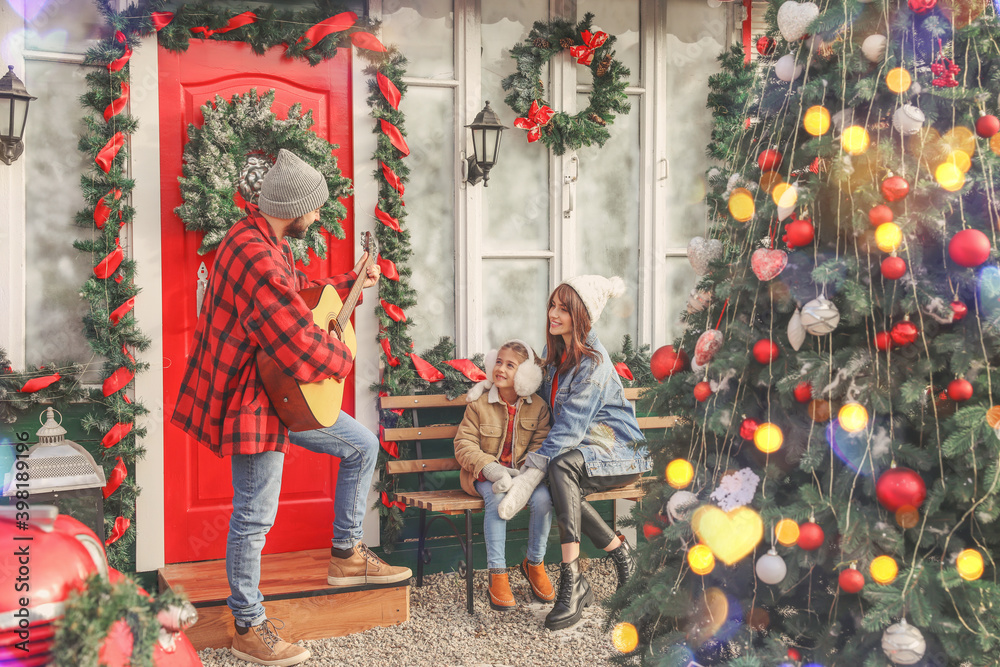 Happy family with guitar near house decorated for Christmas