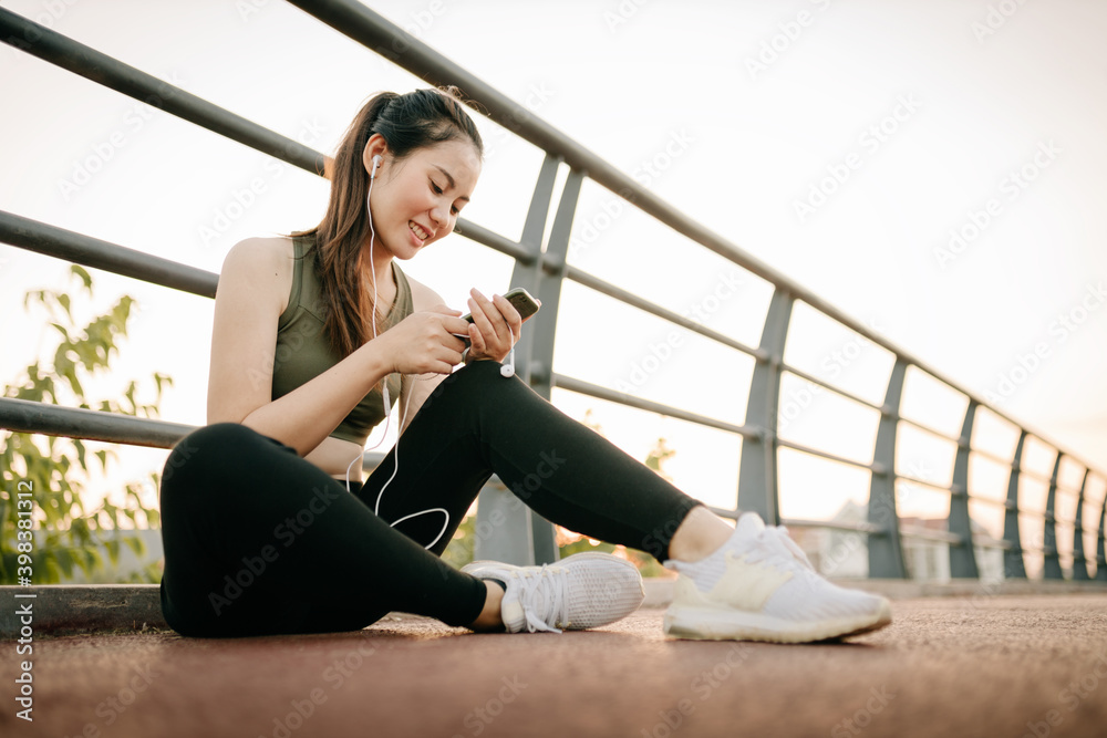 穿着运动服的亚洲美女在阳光公园户外运动时听音乐