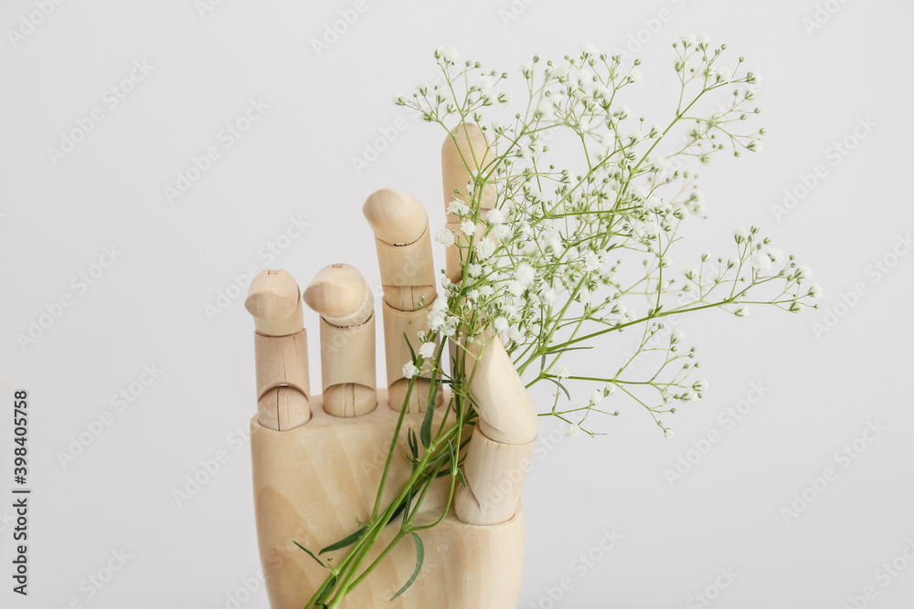 Wooden hand with flowers on light background