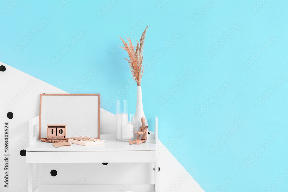 Stylish workplace with blank photo frame near color wall