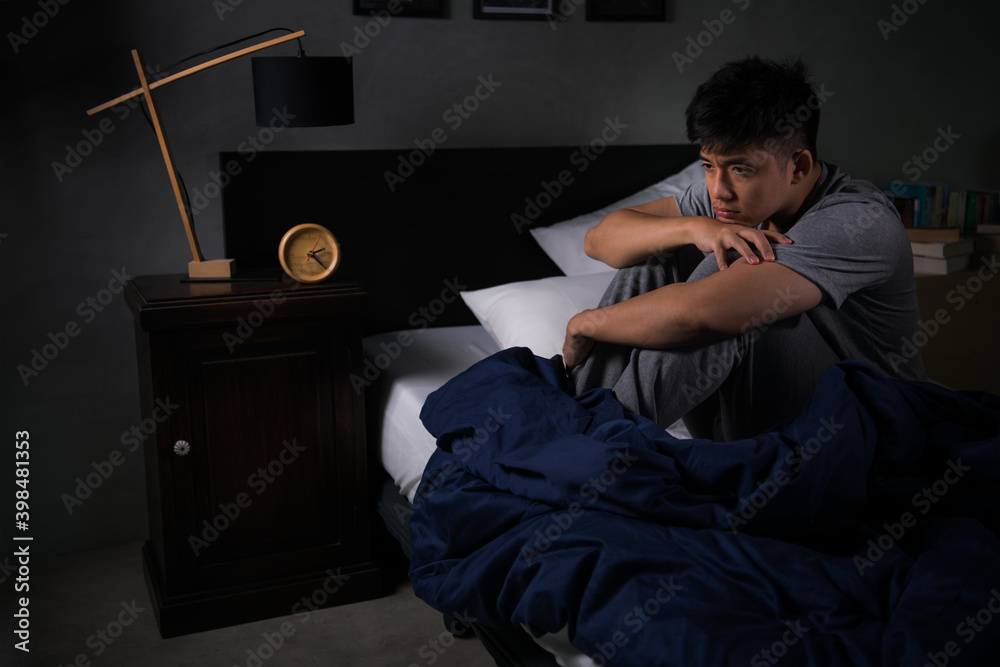 Depressed young man suffering from insomnia sitting in bed..