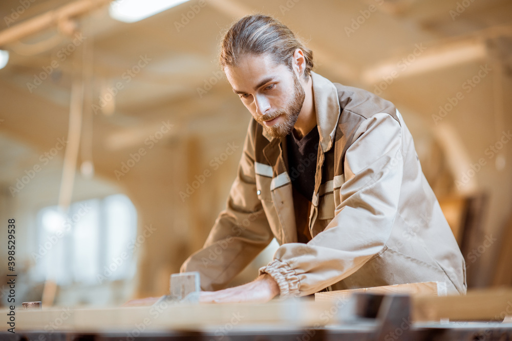 Handsome carpenter in uniform gluing wooden bars with hand pressures at the carpentry manufacturing