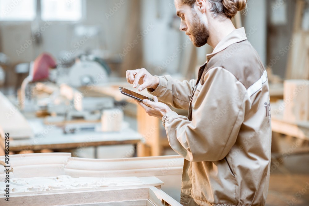 Handsome carpenter working on wooden carvings using a smart phone at the carpentry manufacturing. Co