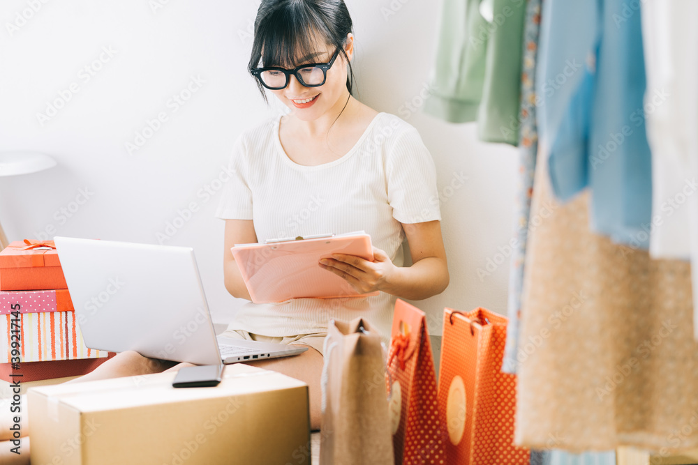 Young Asian businesswoman is sitting on the floor to check her orders from e-commerce sites