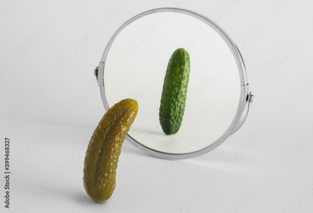 Pickled cucumber looking at its reflection in mirror on light background