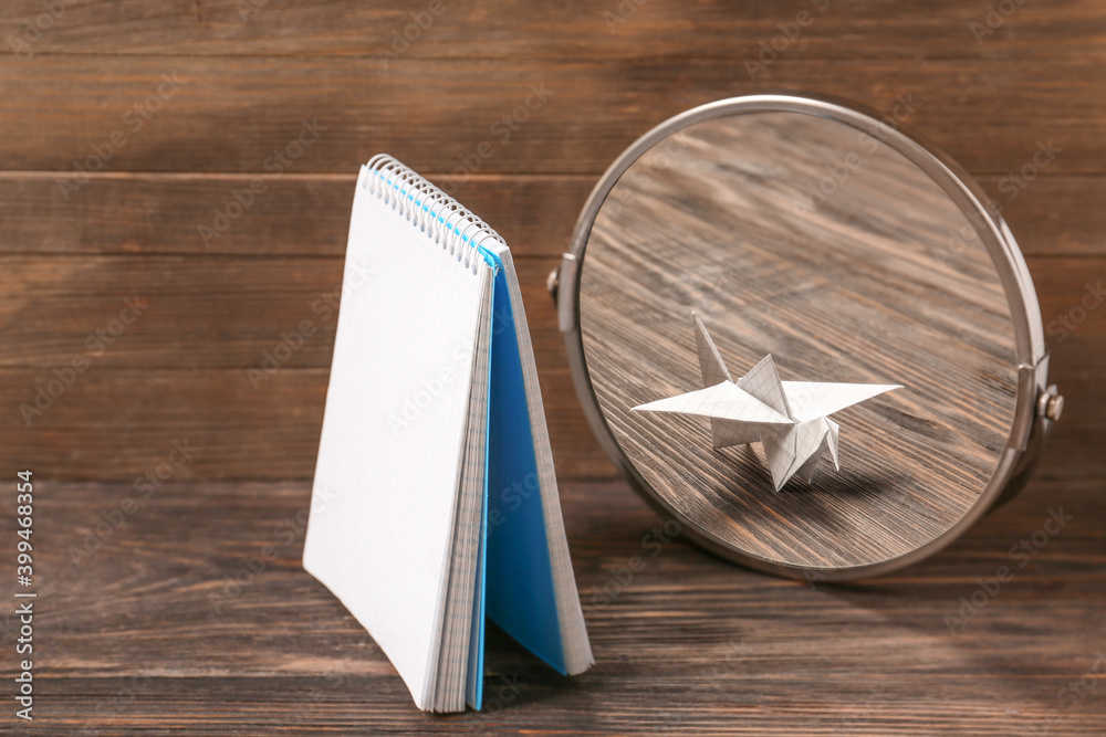 Notebook looking at its reflection in mirror on wooden background