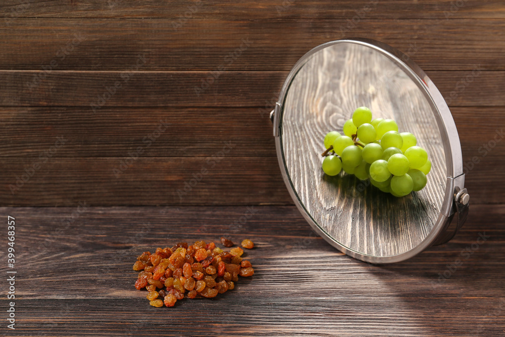 Raisins looking at its reflection in mirror on wooden background