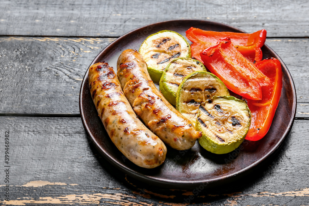 Plate with delicious grilled sausages and vegetables on dark background